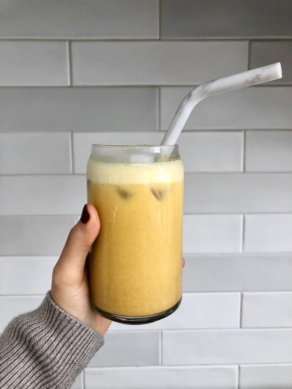 Cashew golden milk latte in a glass  with ice and a marble reusable straw. 