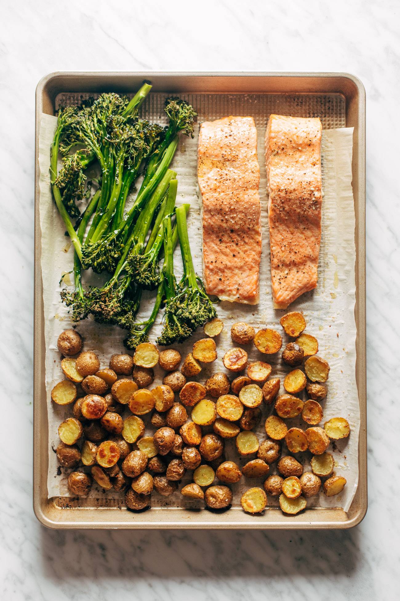 Roasted broccoli, baked salmon, and roasted potatoes on a lined sheet pan. 