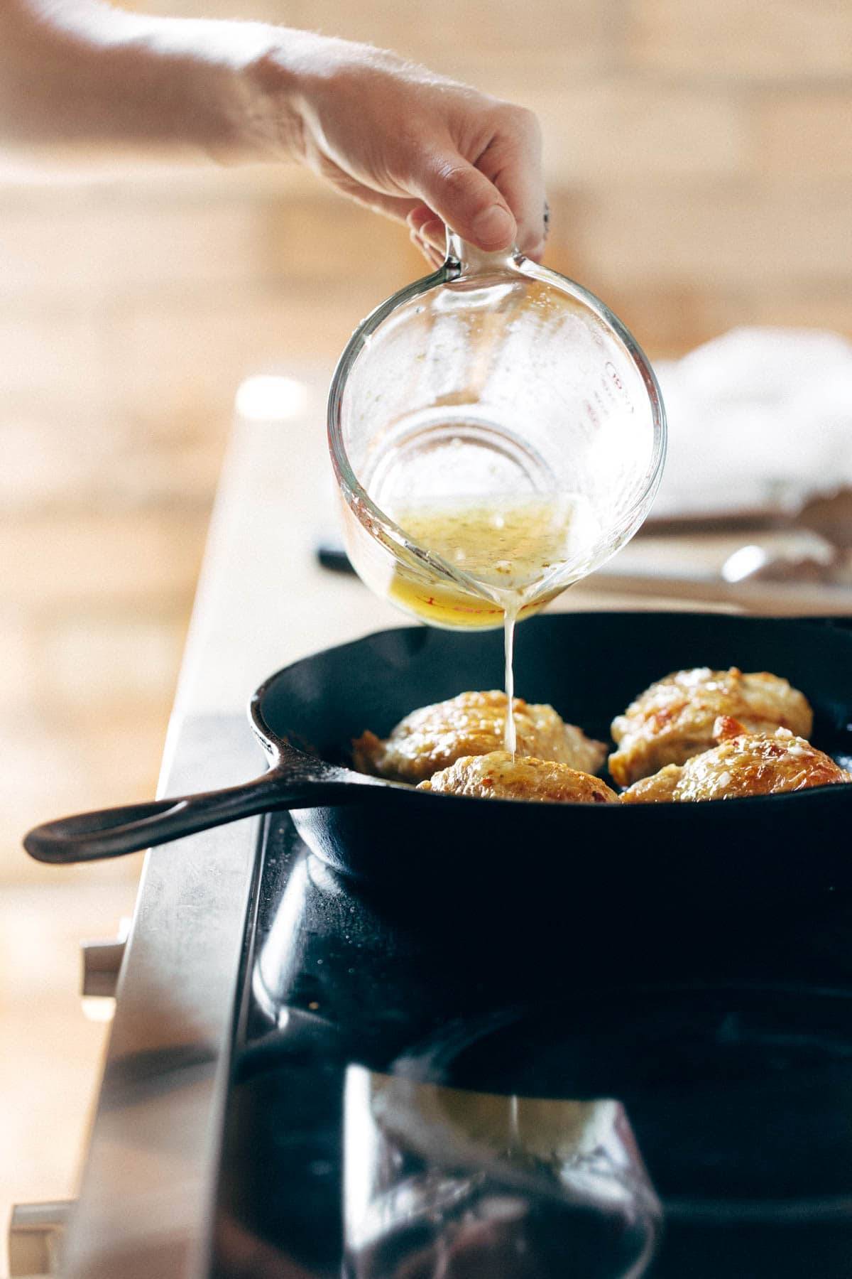 Pouring lemon dressing on chicken in a skillet.