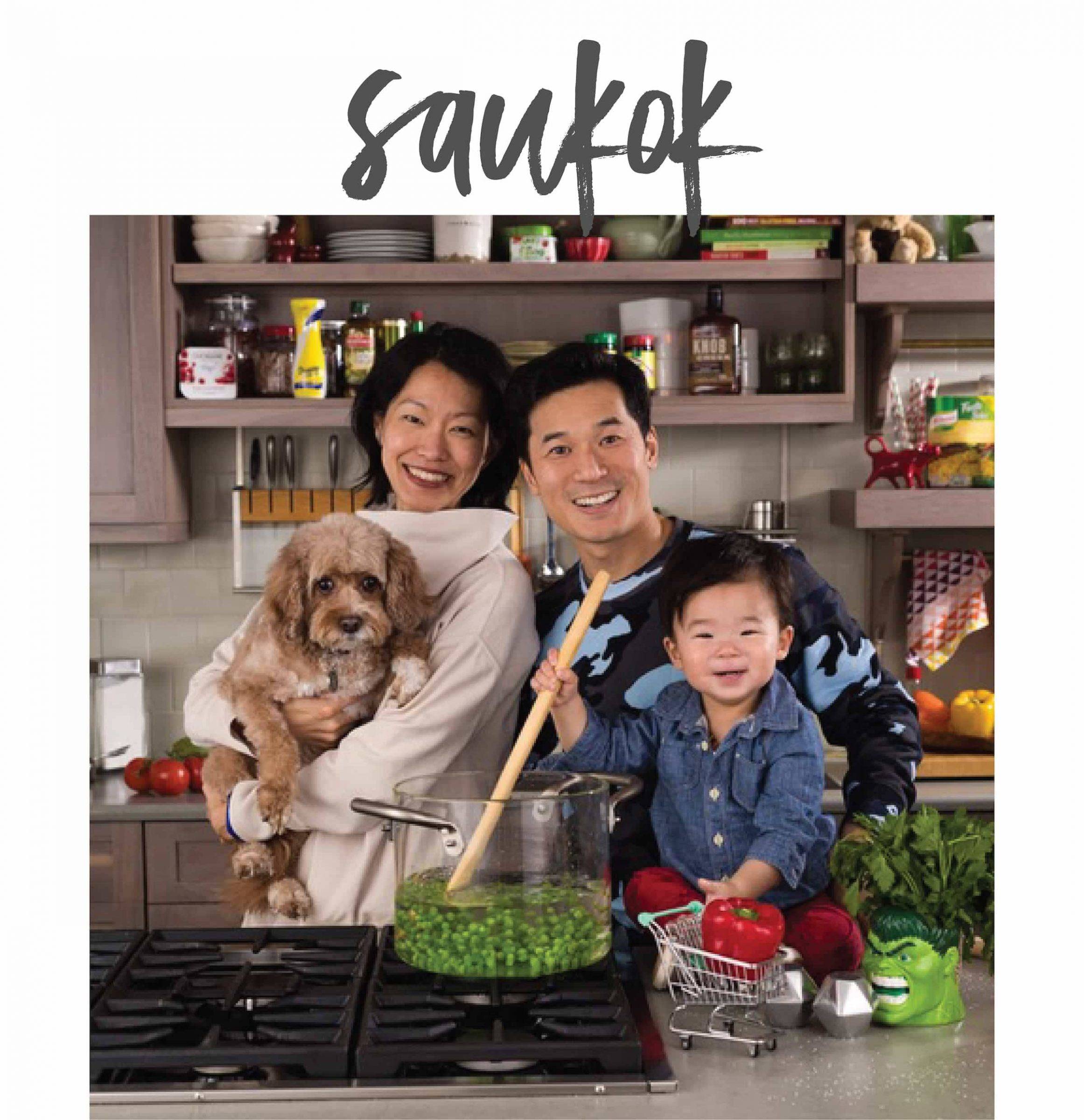 A man, woman, and child in a kitchen with their dog.