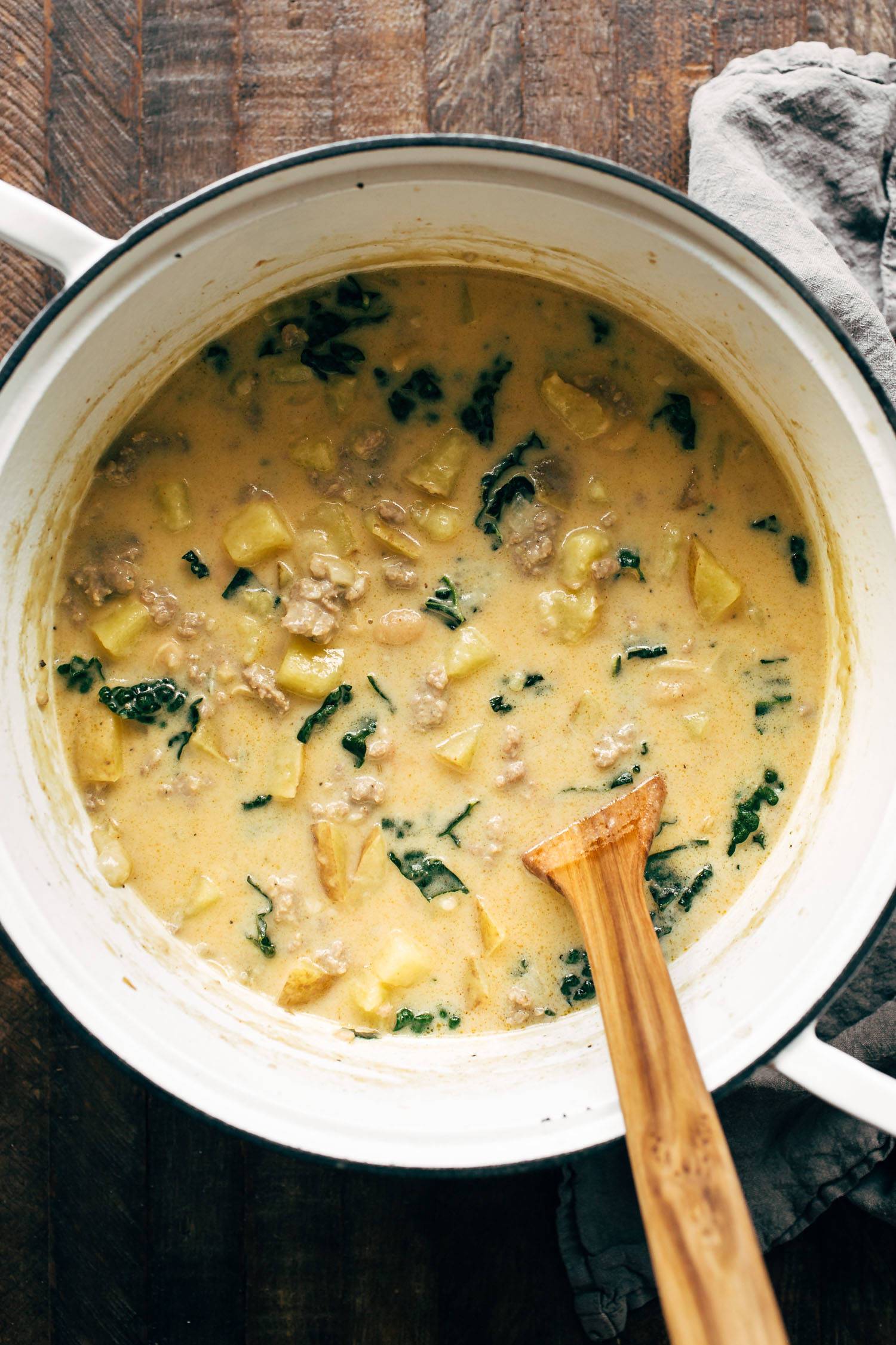 Sausage, kale, and bean soup in a pot with a wooden spoon.