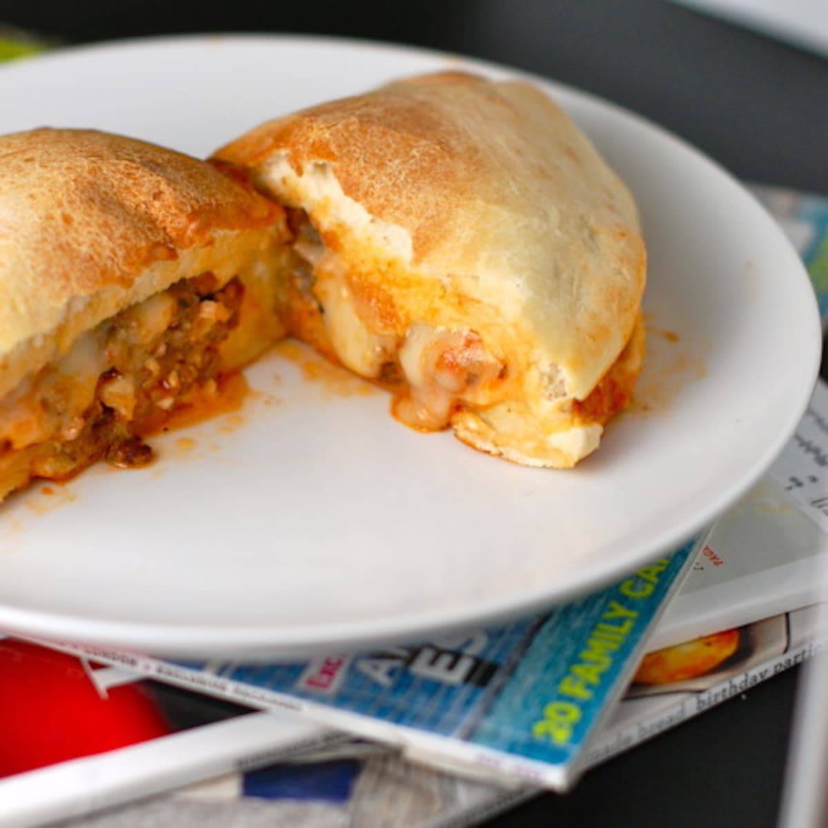 Sausage and mozzarella calzones on a white plate on top of magazines.