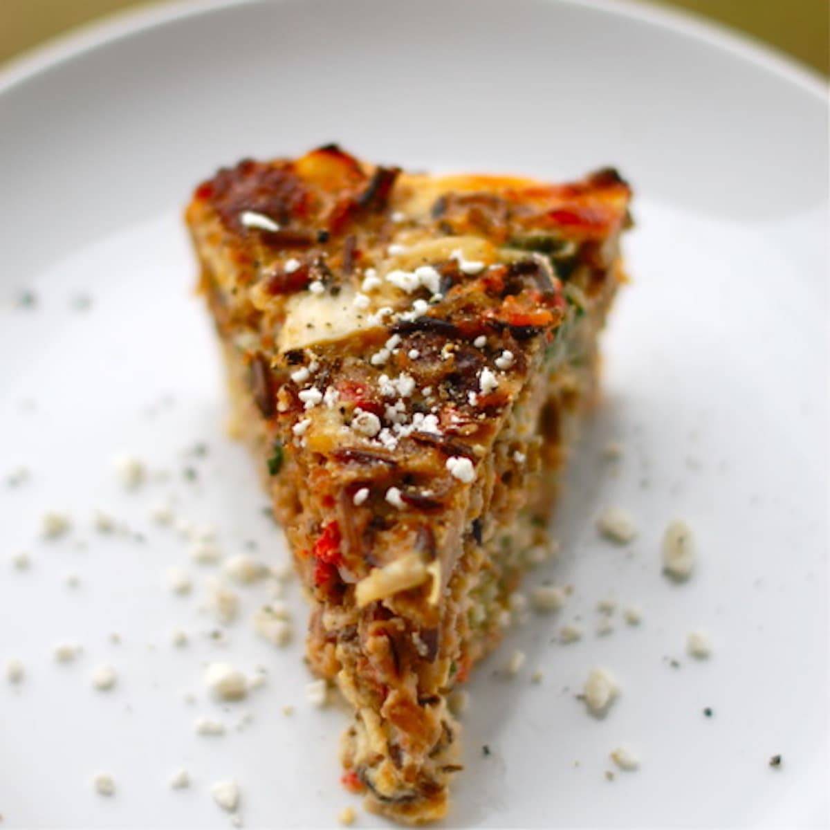 Sausage and red pepper quiche on a white plate.
