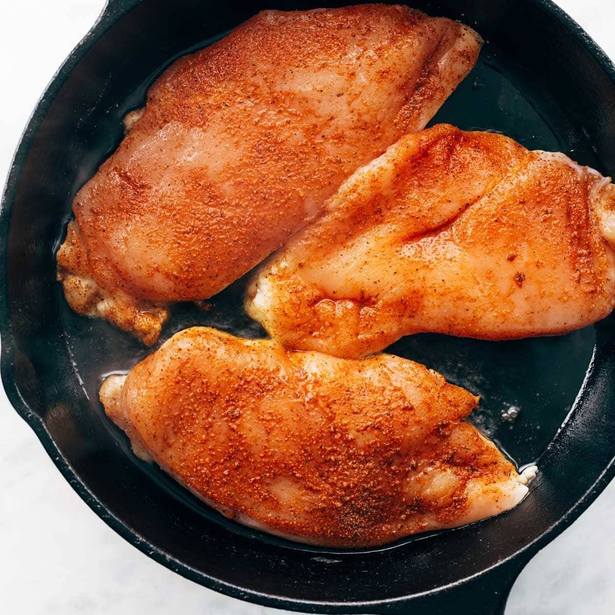 Seasoned chicken breasts in a pan.