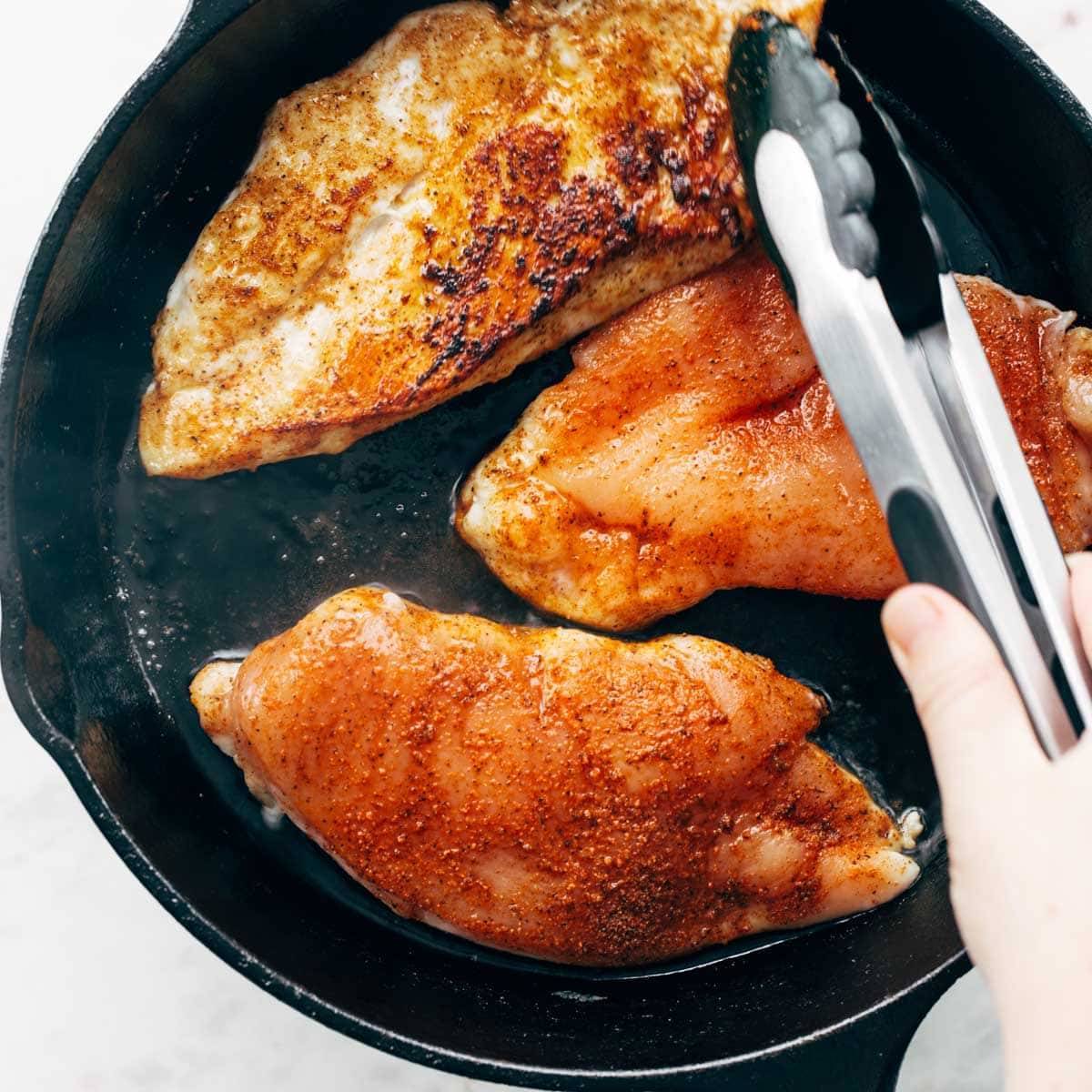 Sautéeing chicken breasts in a pan.