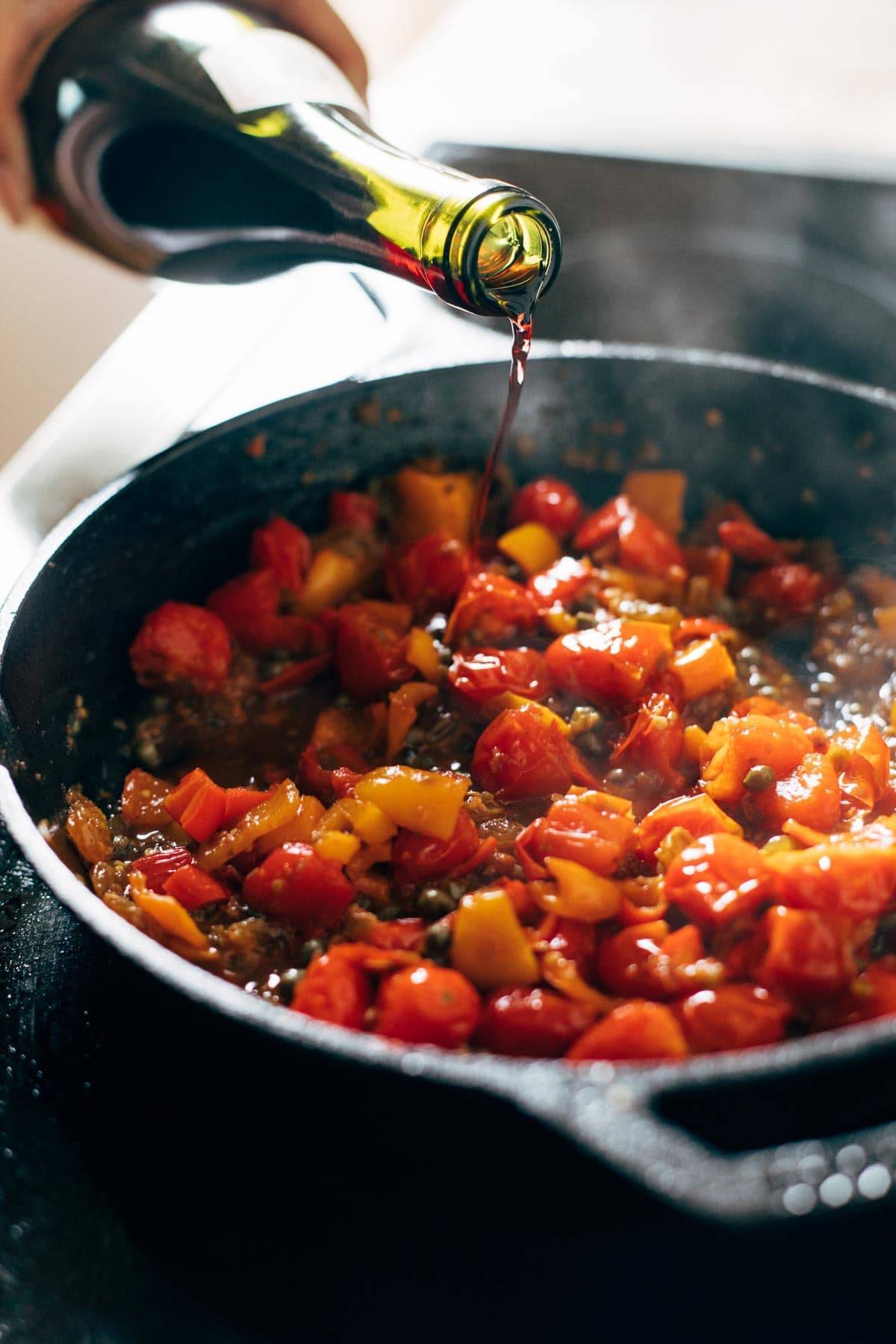 Adding wine to skillet of peppers and tomatoes.
