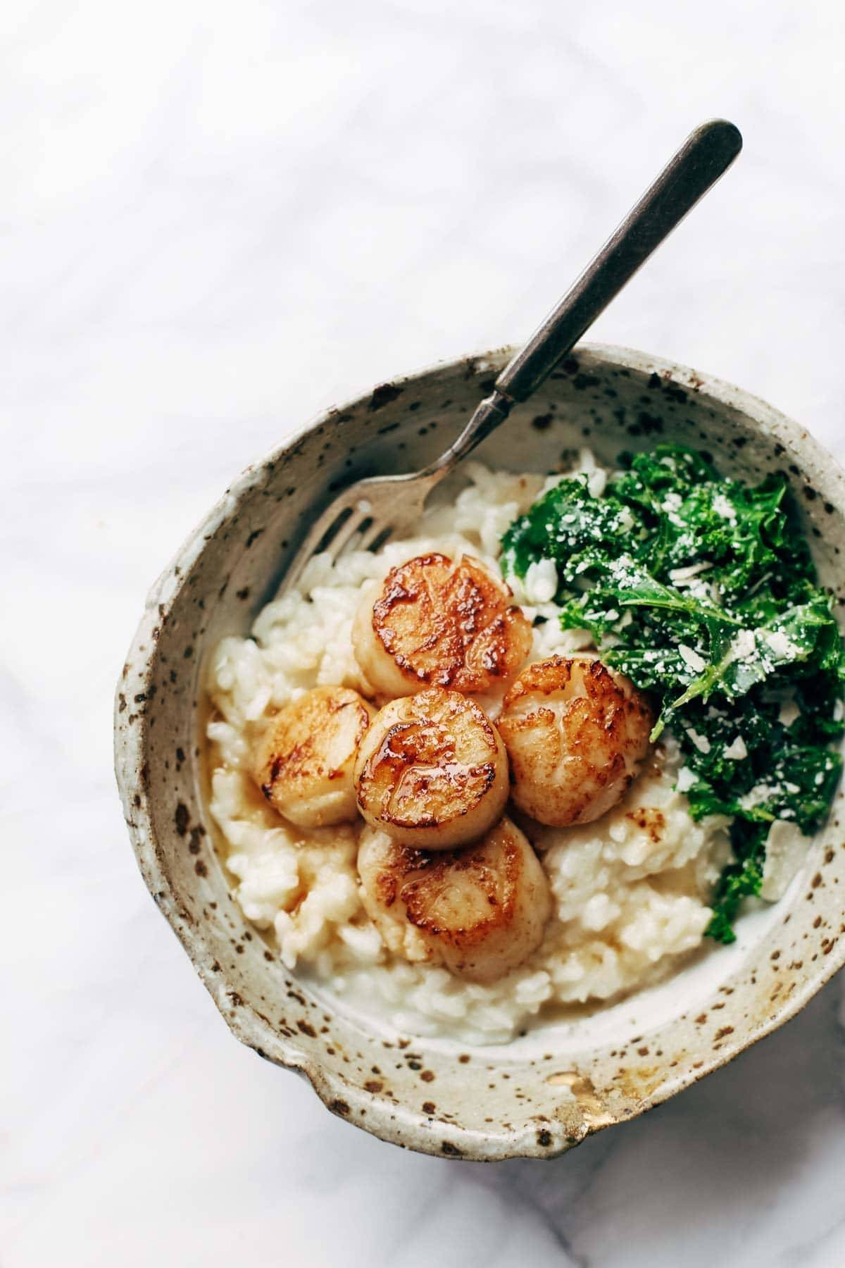 Brown butter scallops in a bowl with kale and risotto. There's a fork in the bowl. 
