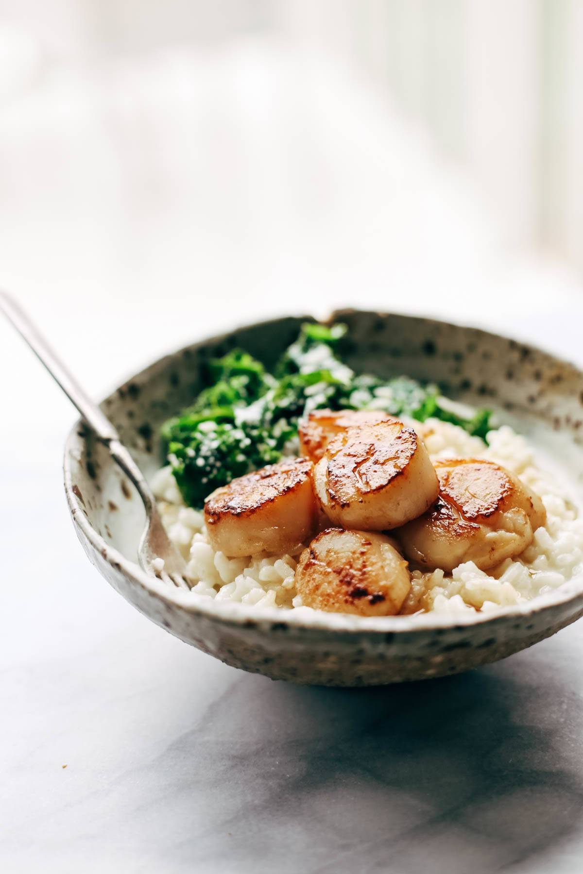 Brown butter scallops in a bowl with a fork, parmesan risotto, and kale. 