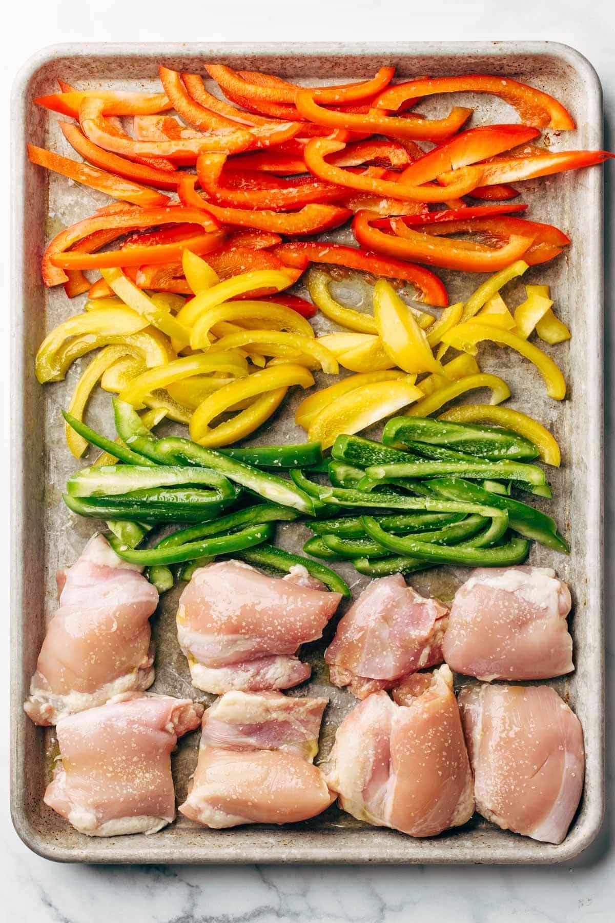 Various colors of peppers on a baking sheet with chicken breasts.