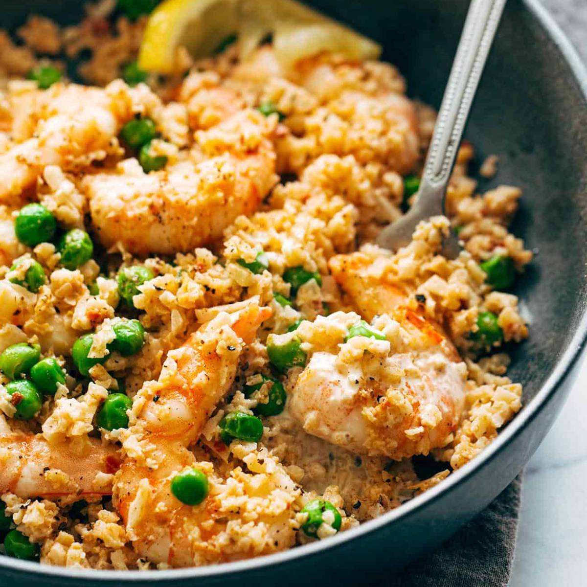 Shrimp, cauliflower rice, and peas in a bowl with a fork