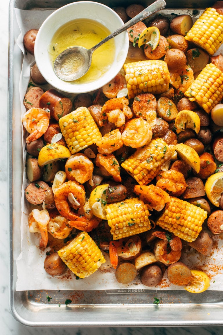 Shrimp, potato and corn mixture on a sheet pan with a side of melted butter in a bowl.