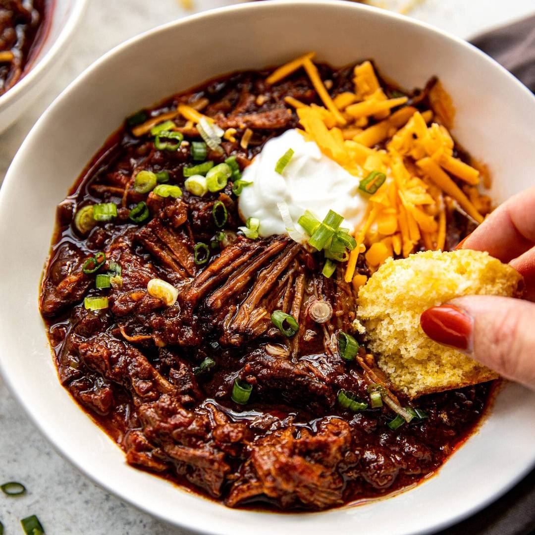 Texas chili in a bowl with cheese, sour cream, and cornbread.