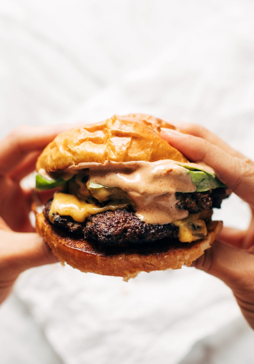 Hands holding a juicy smash burger with sauce.