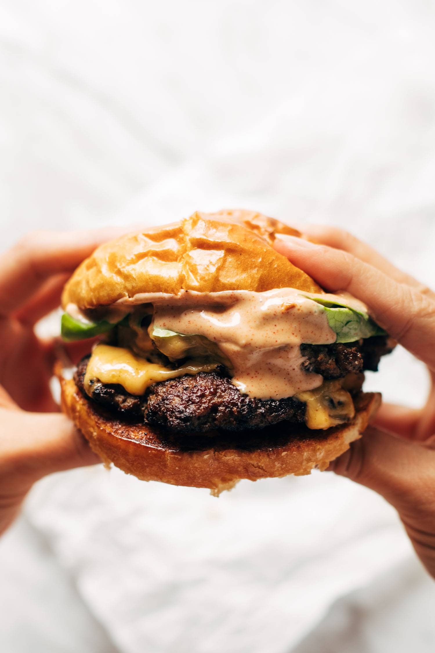 Hands holding a juicy smash burger with sauce.