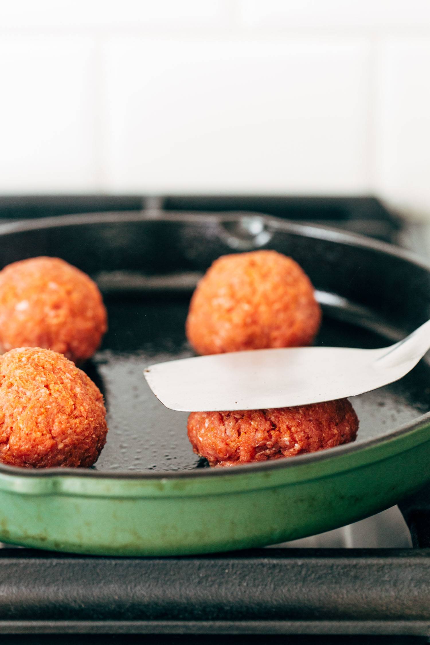 Metal spatula smashing a burger in a pan.