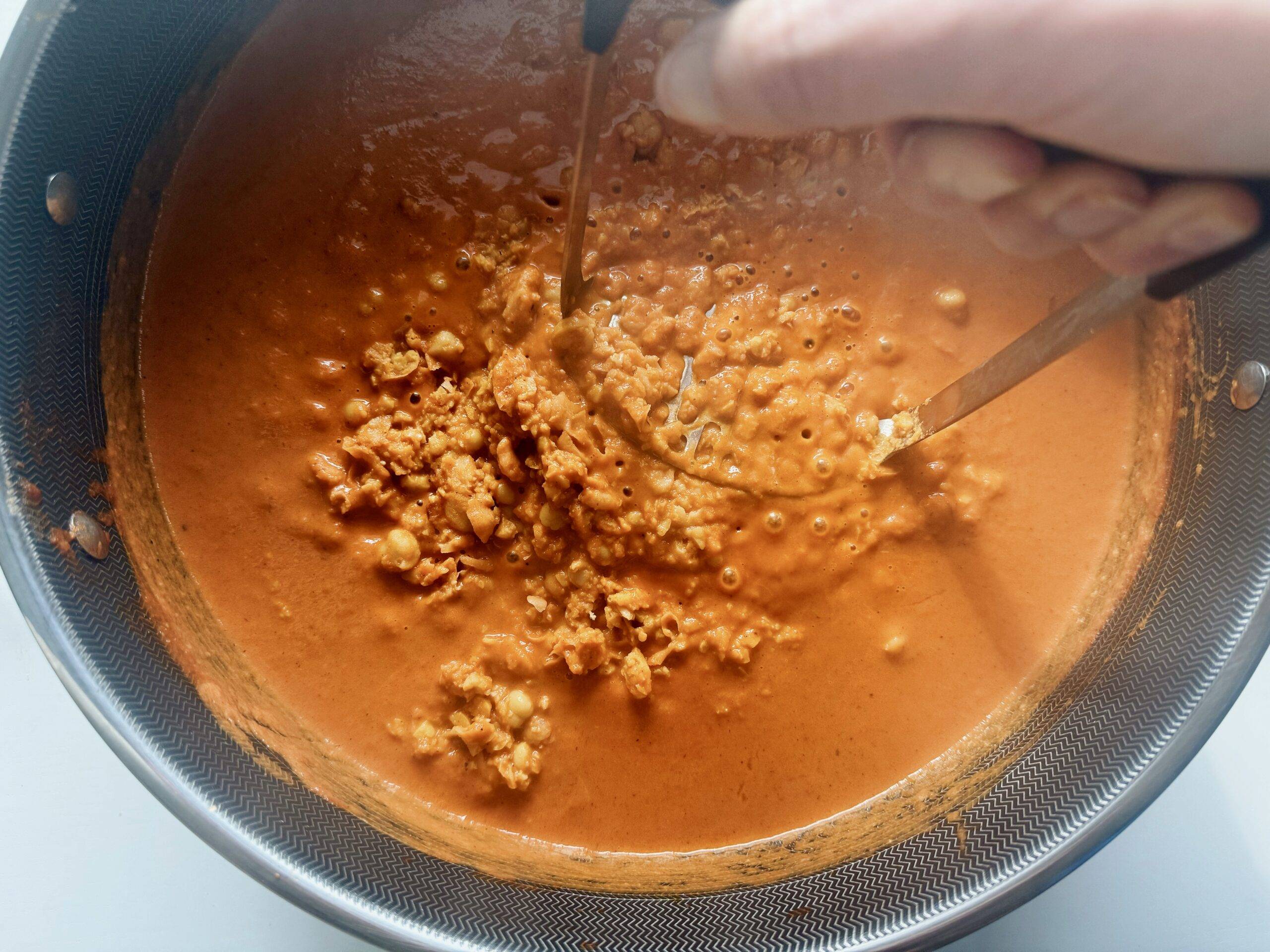 Mashing chickpeas in a pot with sauce.
