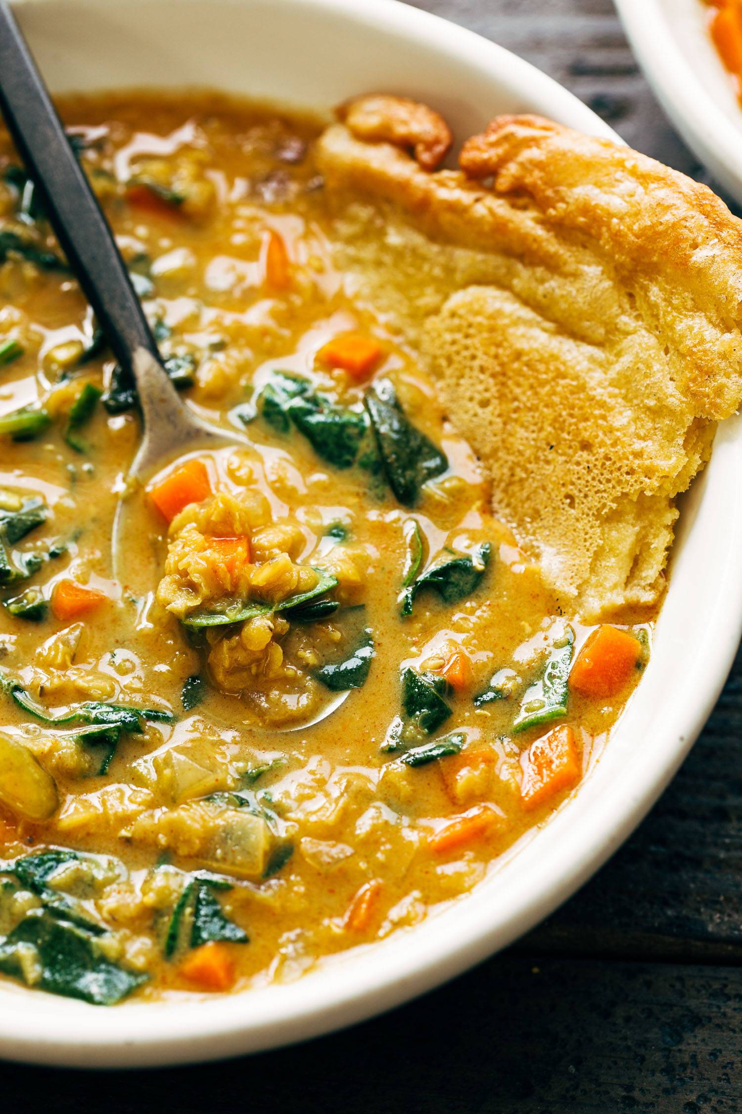 Smoky red lentil soup in a bowl with a metal spoon and socca. 