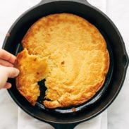 A person breaking off a piece of socca baked in a cast iron skillet.