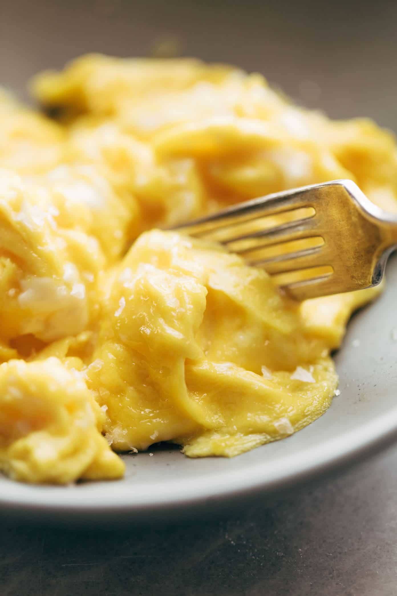 Soft scrambled eggs with a fork on a plate.