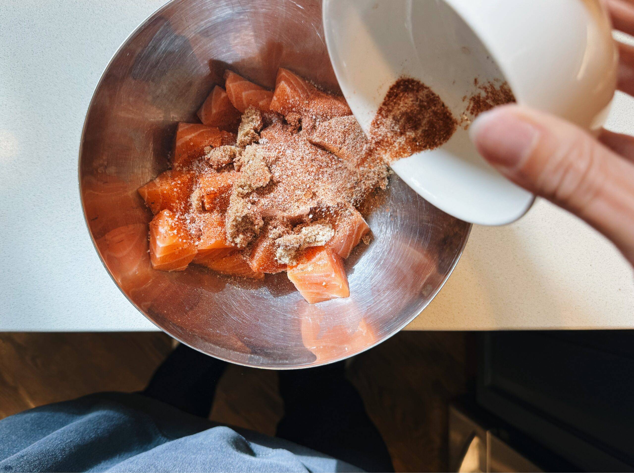 Sprinkling spices on cubed salmon in a bowl.