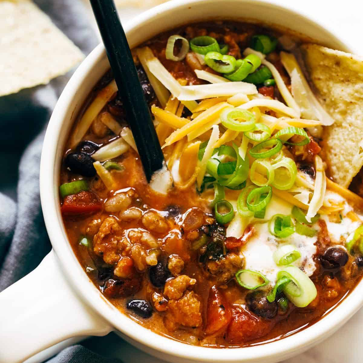 Turkey chili in a bowl with cheese and green onions.