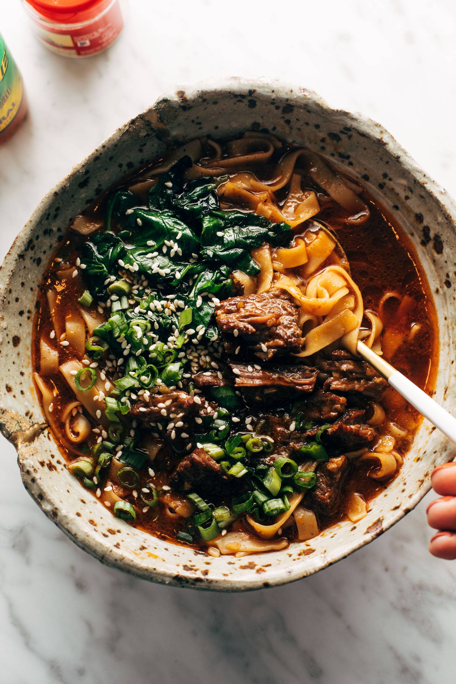 Short rib noodle soup in a bowl with white hand holding a spoon