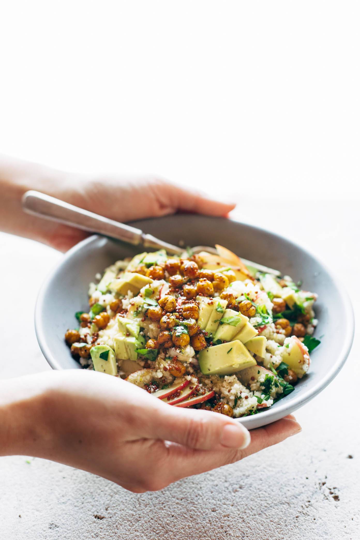 Hands holding Spring Detox Cauliflower Salad in a bowl with a fork.