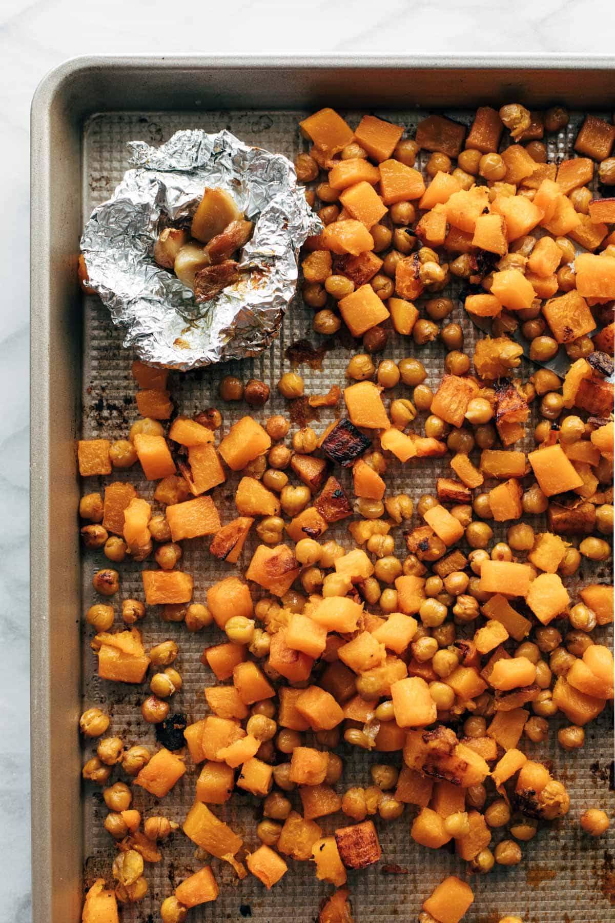 Roasted squash, chickpeas, and garlic on a sheet pan.