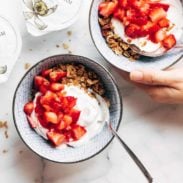 A bowl of granola with yogurt and strawberries on top.