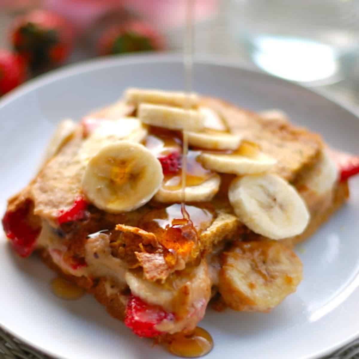 Stuffed French Toast with strawberries, bananas, and maple syrup drizzle on a white plate.