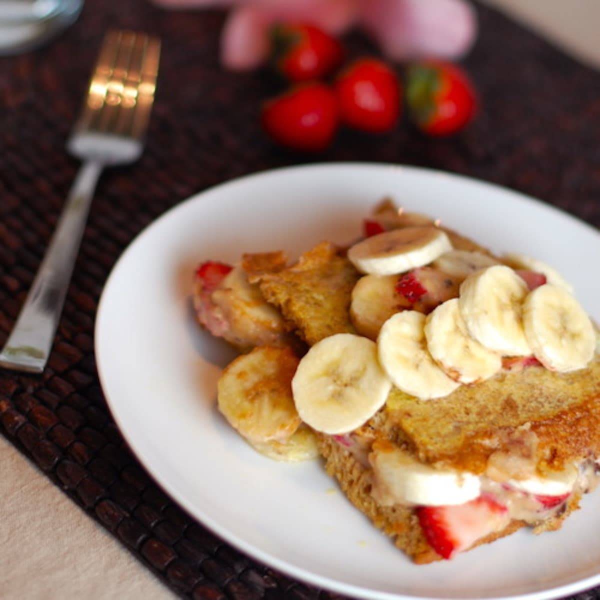 Stuffed French Toast with strawberries, bananas, and maple syrup on a plate with a fork.