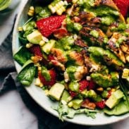 Spinach salad full of corn, strawberries, avocado, and chicken in a bowl on a table with a tablecloth.