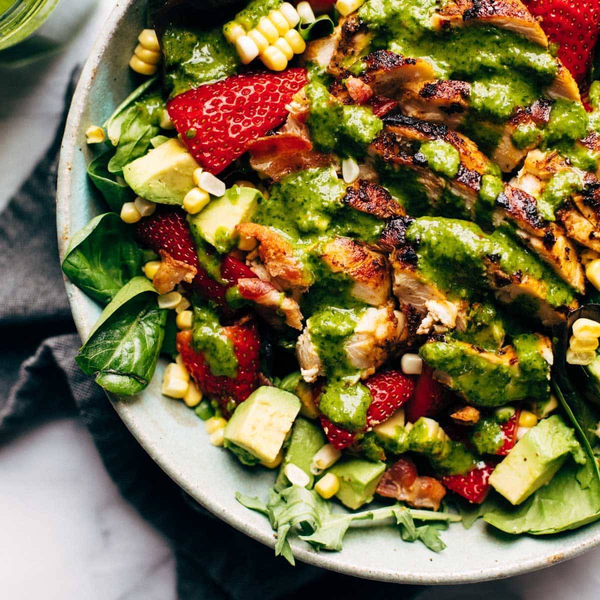 Spinach salad full of corn, strawberries, avocado, and chicken in a bowl on a table with a tablecloth.