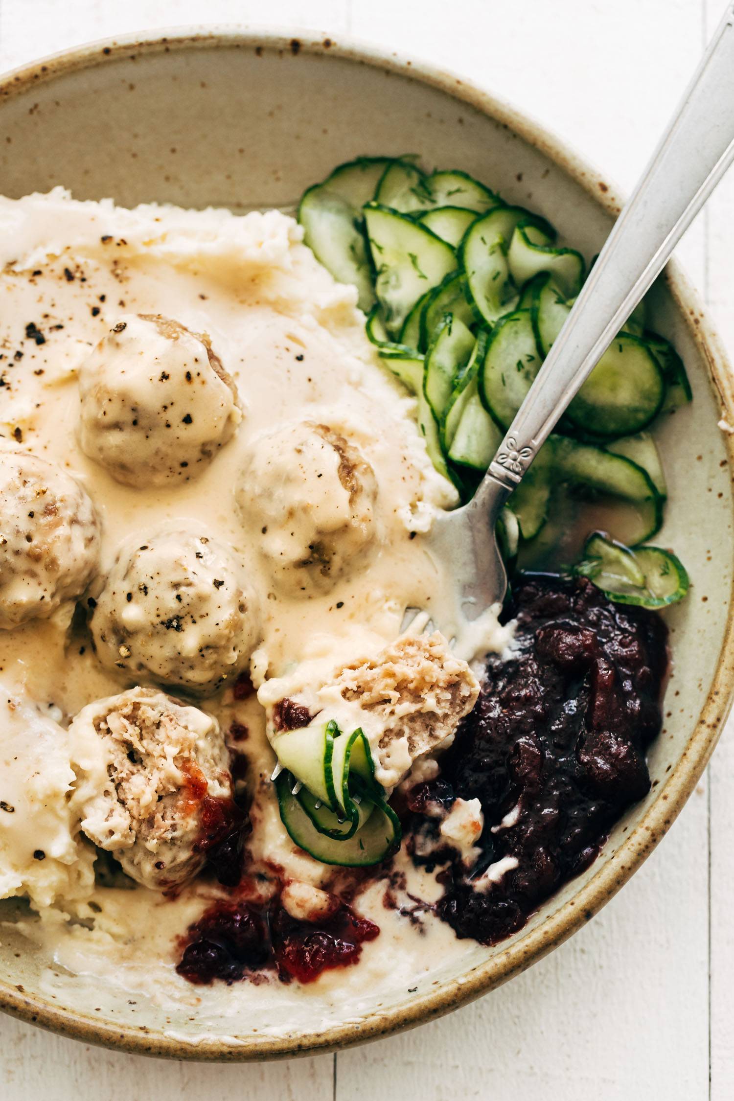 Swedish meatballs in a bowl with cucumbers and cranberries.