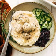 Swedish meatballs in a bowl with gravy, cranberries, and cucumbers