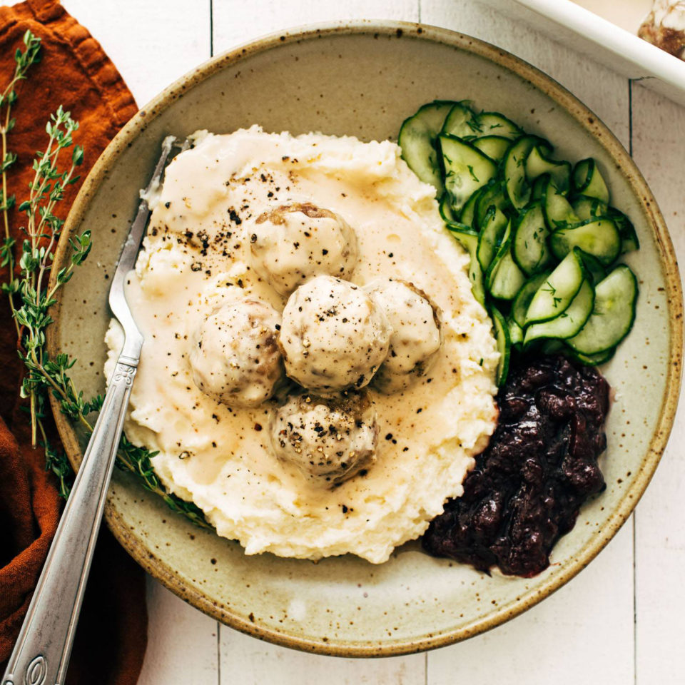 Swedish meatballs in a bowl with gravy, cranberries, and cucumbers