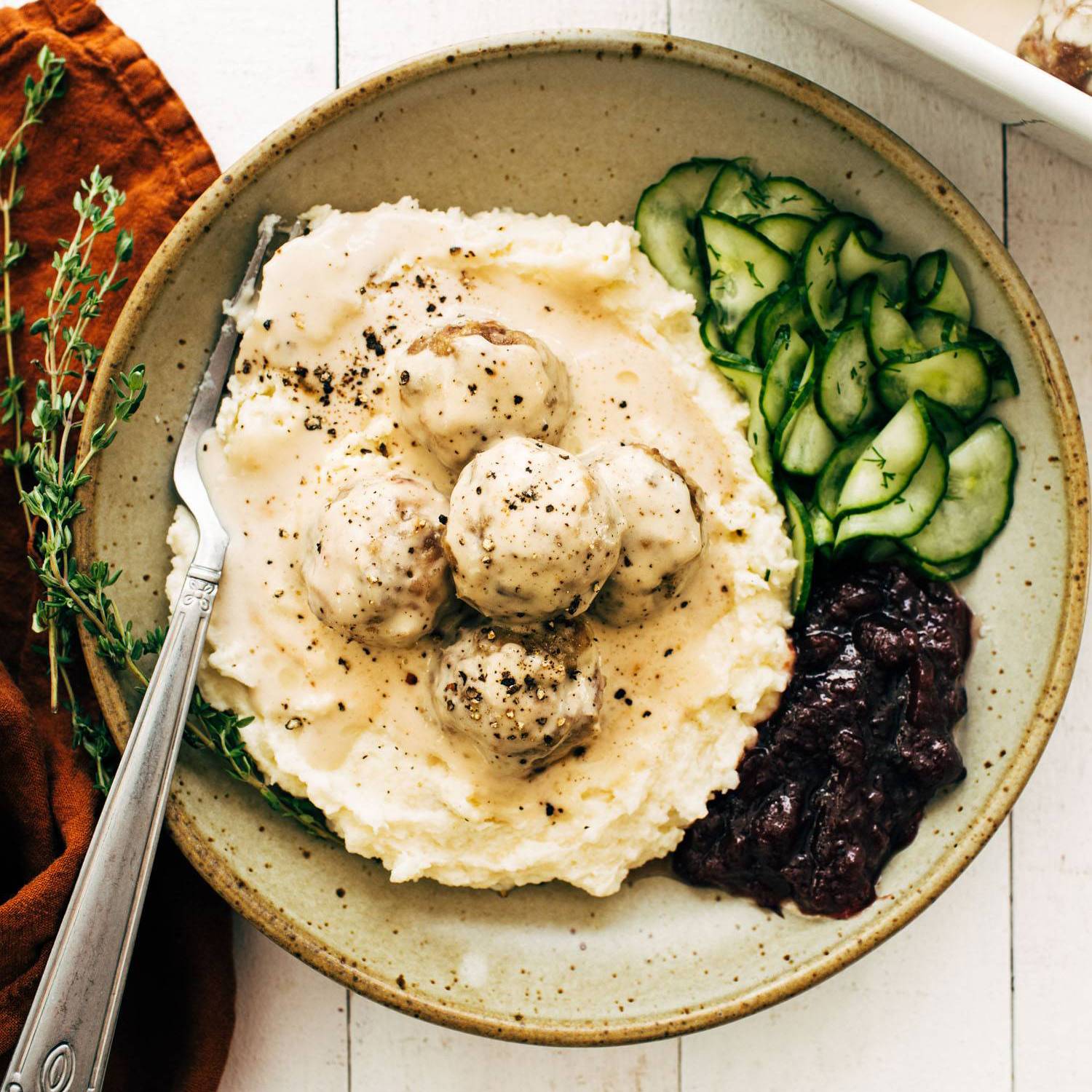 Swedish meatballs in a bowl with cranberries and cucumbers.
