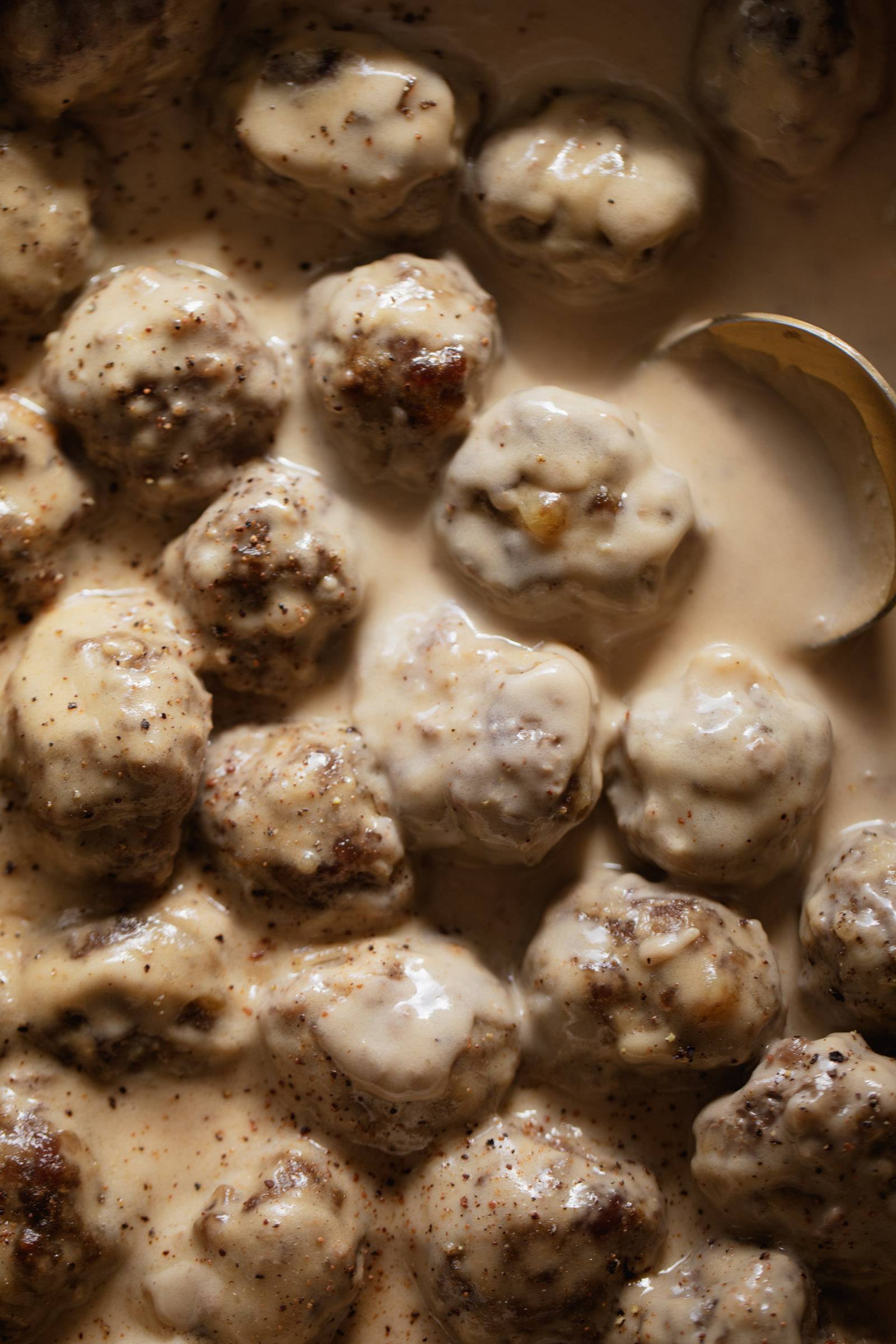 Swedish Meatballs in a pan with gravy and a spoon.