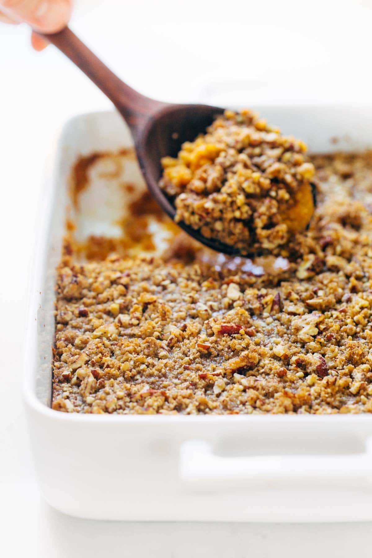 Sweet Potato Casserole with a crunchy brown sugar topping with a wooden spoon