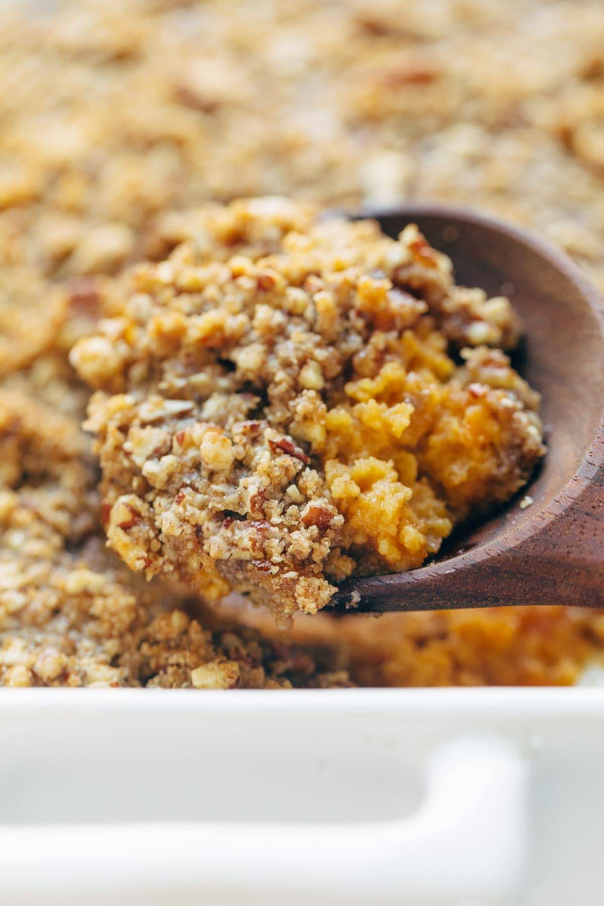 Sweet Potato Casserole with a crunchy brown sugar topping in a wooden spoon
