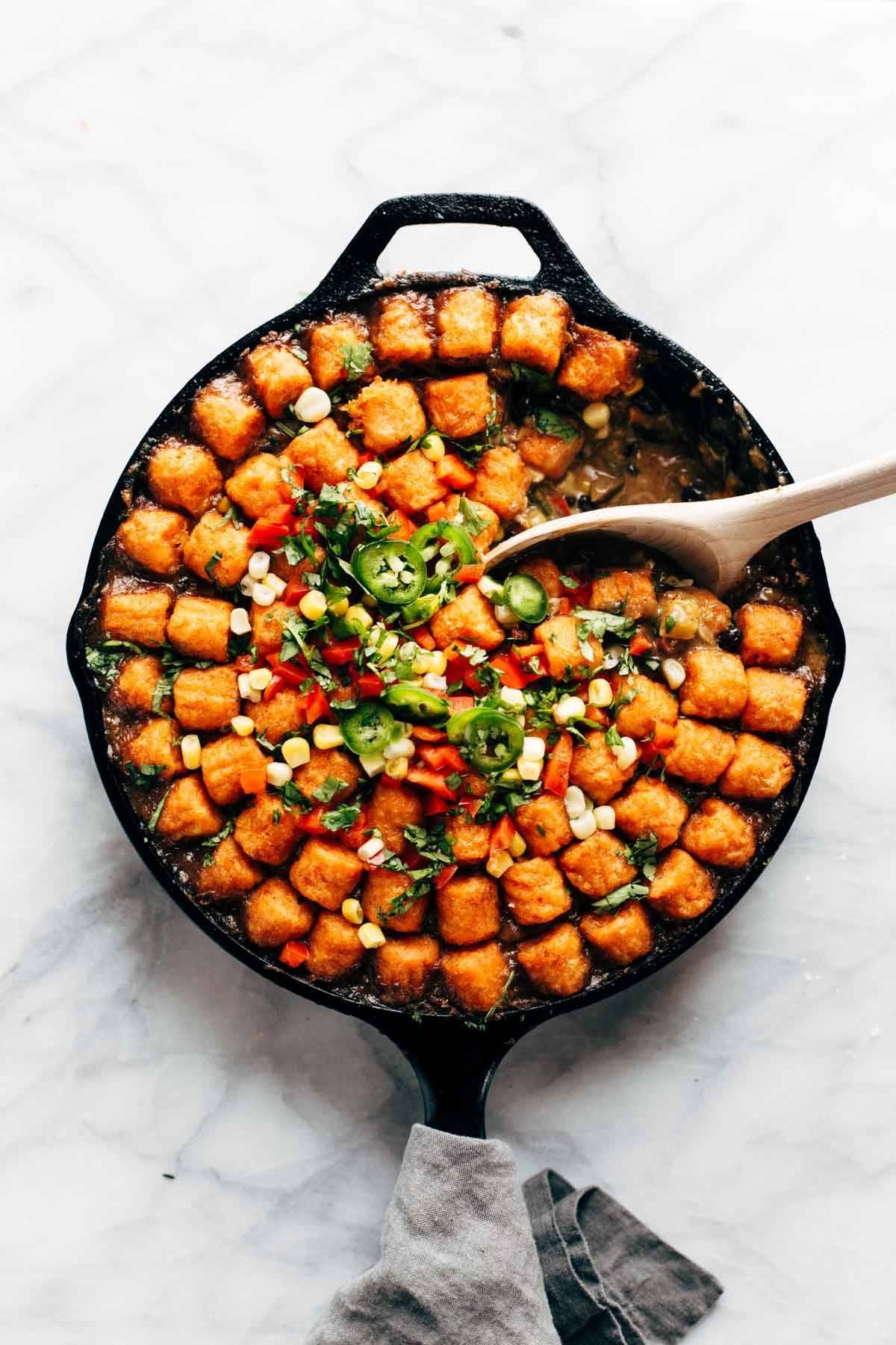 sweet potato tater tot hotdish in a skillet with a wooden spoon