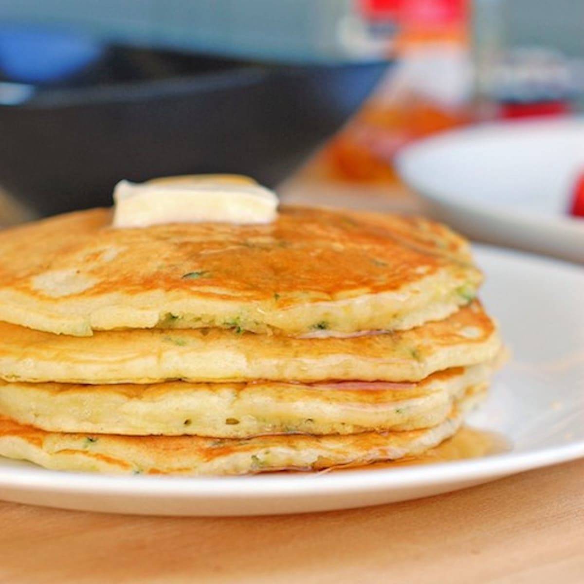 Stack of zucchini pancakes with butter and maple syrup on a plate.