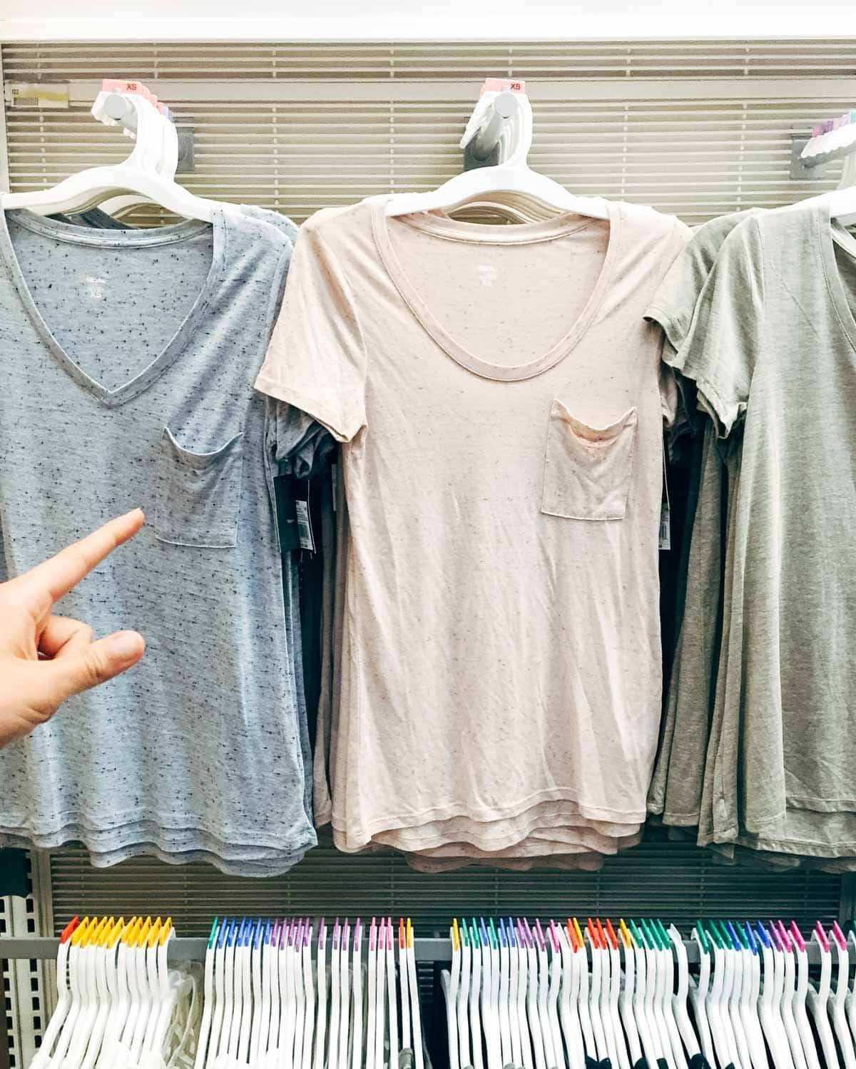 Hand pointing to a cream colored shirt on a rack.