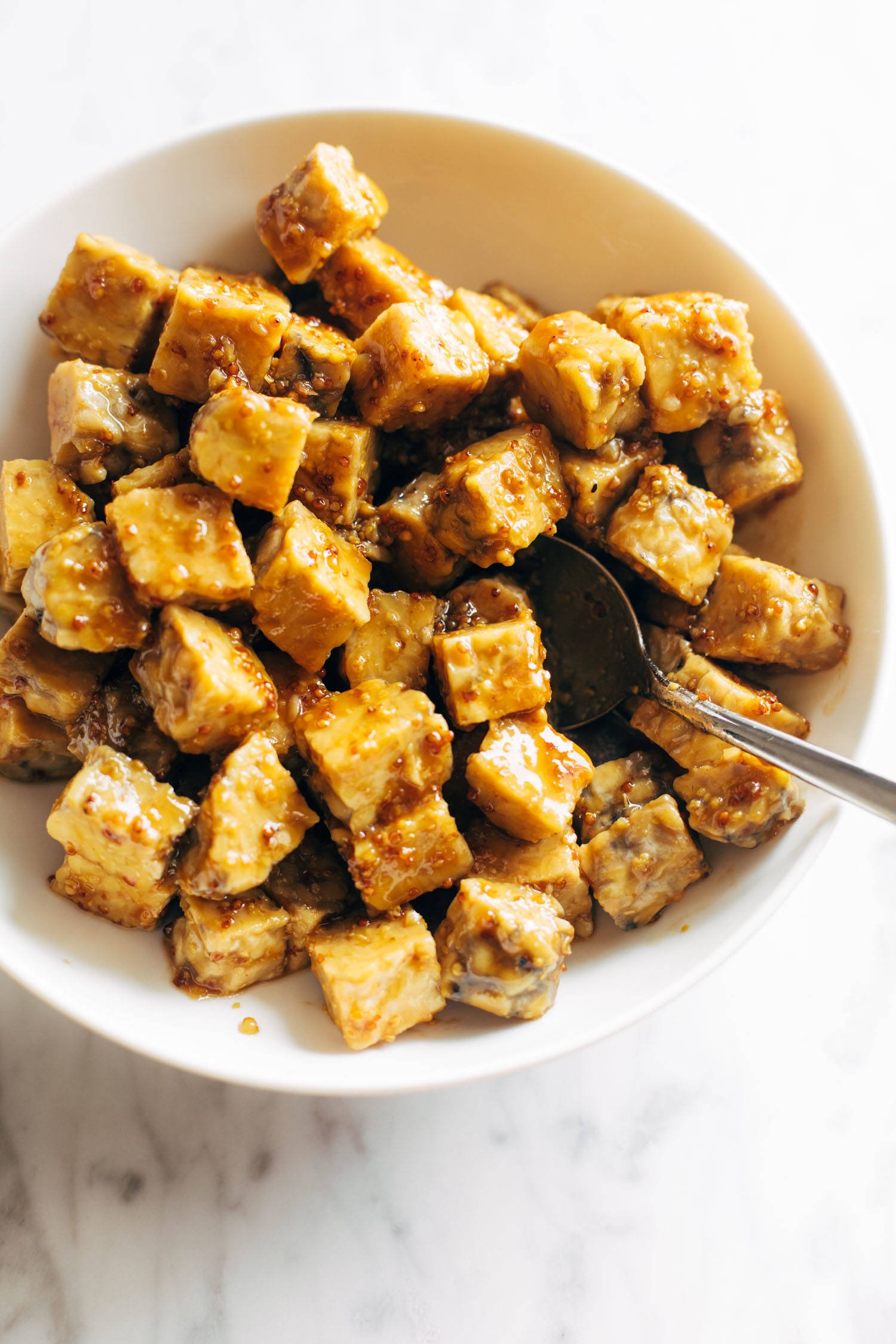 Maple mustard tempeh in a white bowl with a spoon. 