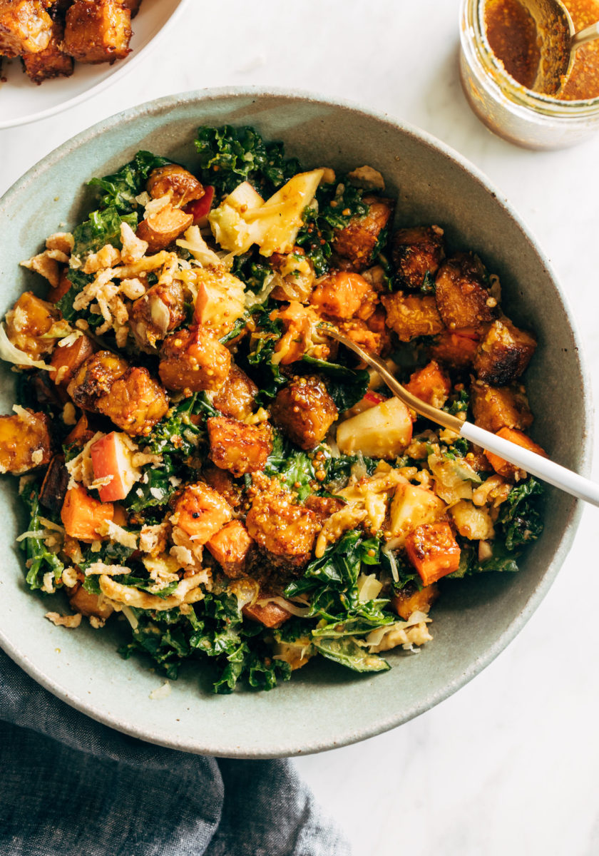 Crispy tempeh with green leafy vegetables in a bowl with a spoon.