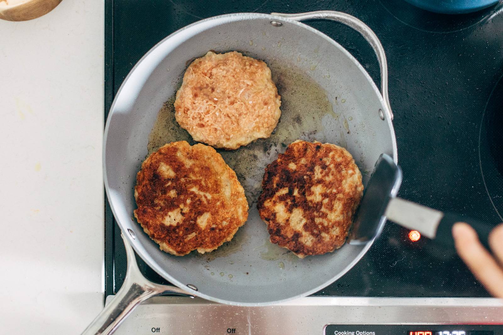 Cooking and flipping chicken burgers in a pan.