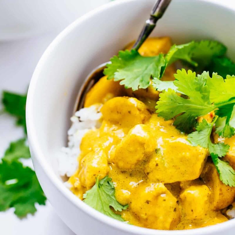 A small bowl of curry chicken on a bed of white rice topped with cilantro.