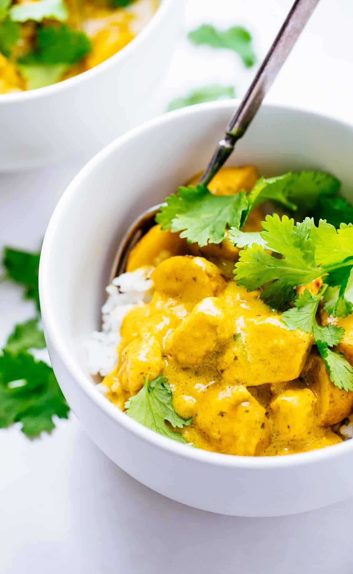 A small bowl of curry chicken on a bed of white rice topped with cilantro.