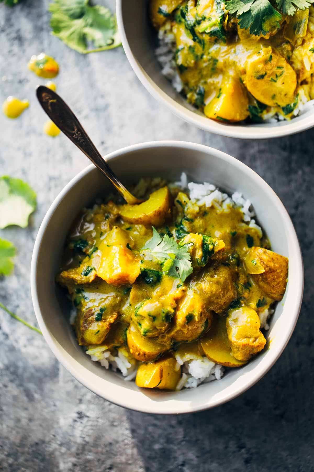 Homemade yellow curry with potatoes and rice in a bowl with a fork. 