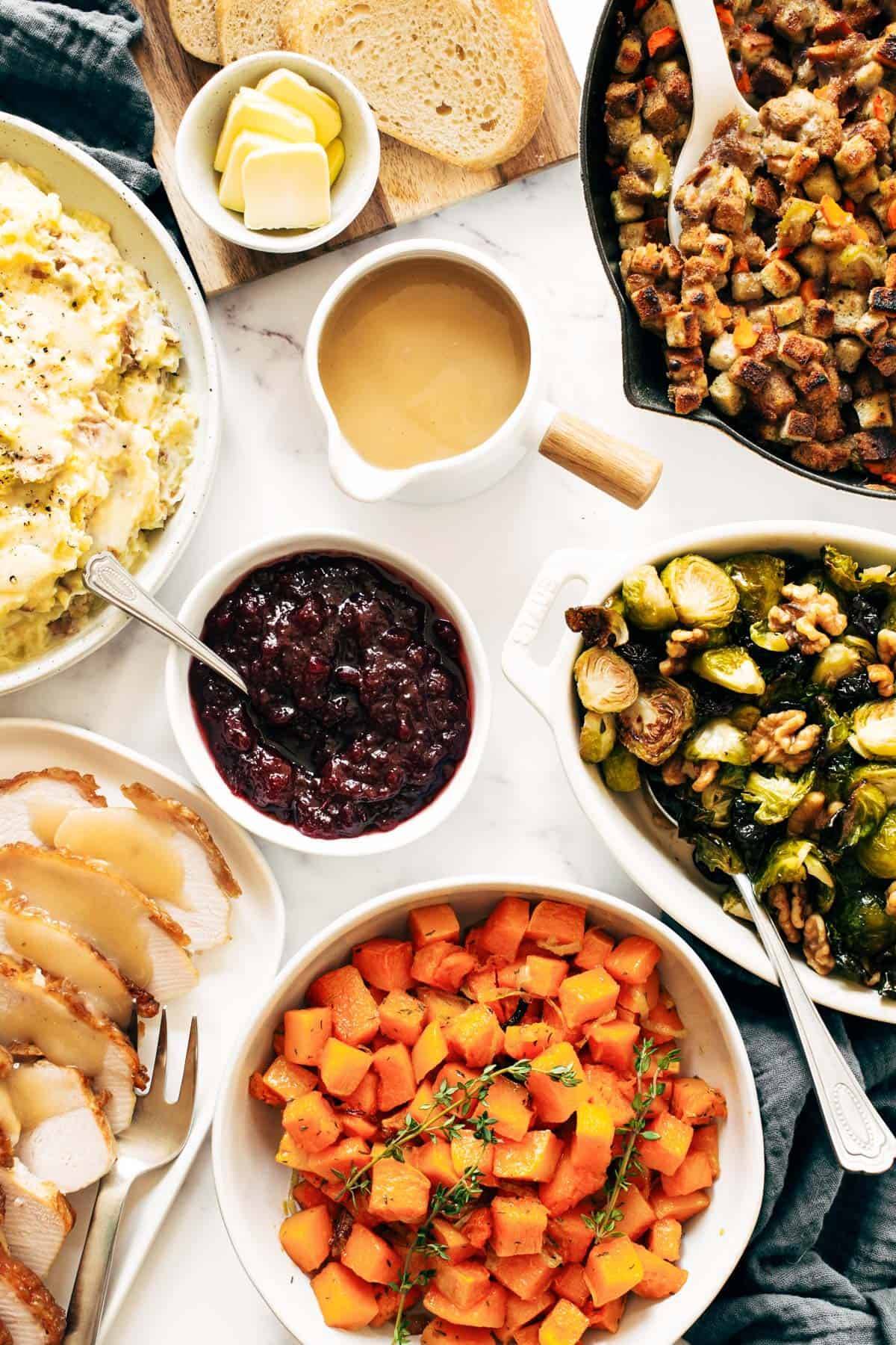 Thanksgiving spread with stuffing, gravy, cranberries, squash, turkey brussels sprouts, and potatoes.